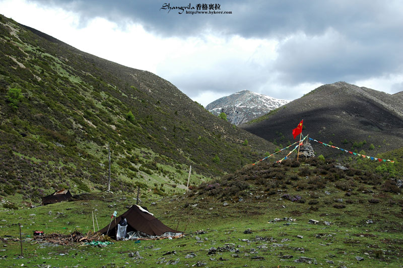 穿越香格里拉(21): 无名山山腰玛尼堆上插着的鲜艳国旗，在浓云雪山的衬托下格外醒目<br>这在今年颇不平静的藏区，似乎别有一番象征意义