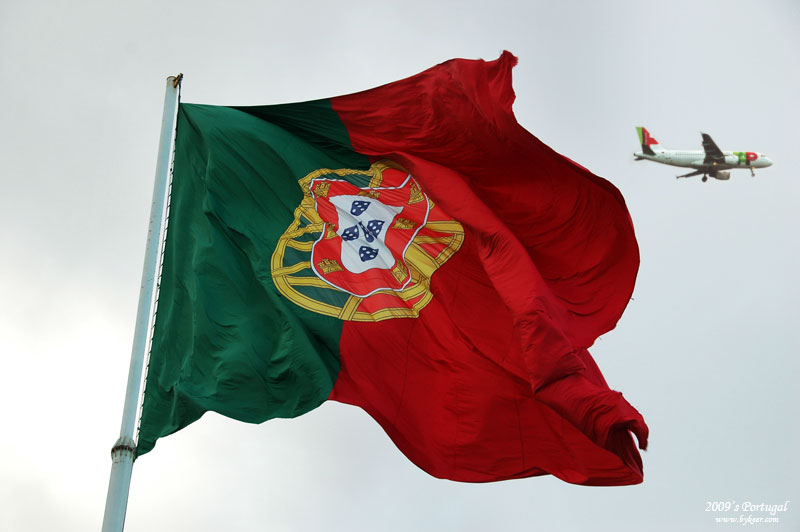 炫色葡萄牙(58): Parque Eduardo VII广场上空飘扬的葡萄牙国旗，纪念20世纪初共和革命的胜利。<br>国旗上，绿色代表民族希望，红色代表为民族希望而献身者的鲜血。<br>国徽是拥有黄道、赤道、两条纬线、一条子午线的浑仪和嵌套有蓝色小盾的葡萄牙式盾牌。<br>正如红绿相间的国旗一般，葡萄牙是一个拥有绚烂风情和缤纷色彩的古老国度。<br>Cabo da Roca的湛蓝海水，Cascais的缤纷海岸，Lisboa、Sintra的瓦红屋顶和精致宫殿，<br>还有无数招展怒放的深蓝绛紫色花朵，是这次葡萄牙短暂行程的最深刻记忆。